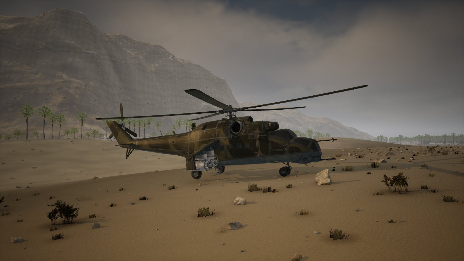 A Mi-24 Hind attack helicopter in two-tone camouflage parked on the sand at Khasab, rocket pods under its stub wings, the mountains behind.